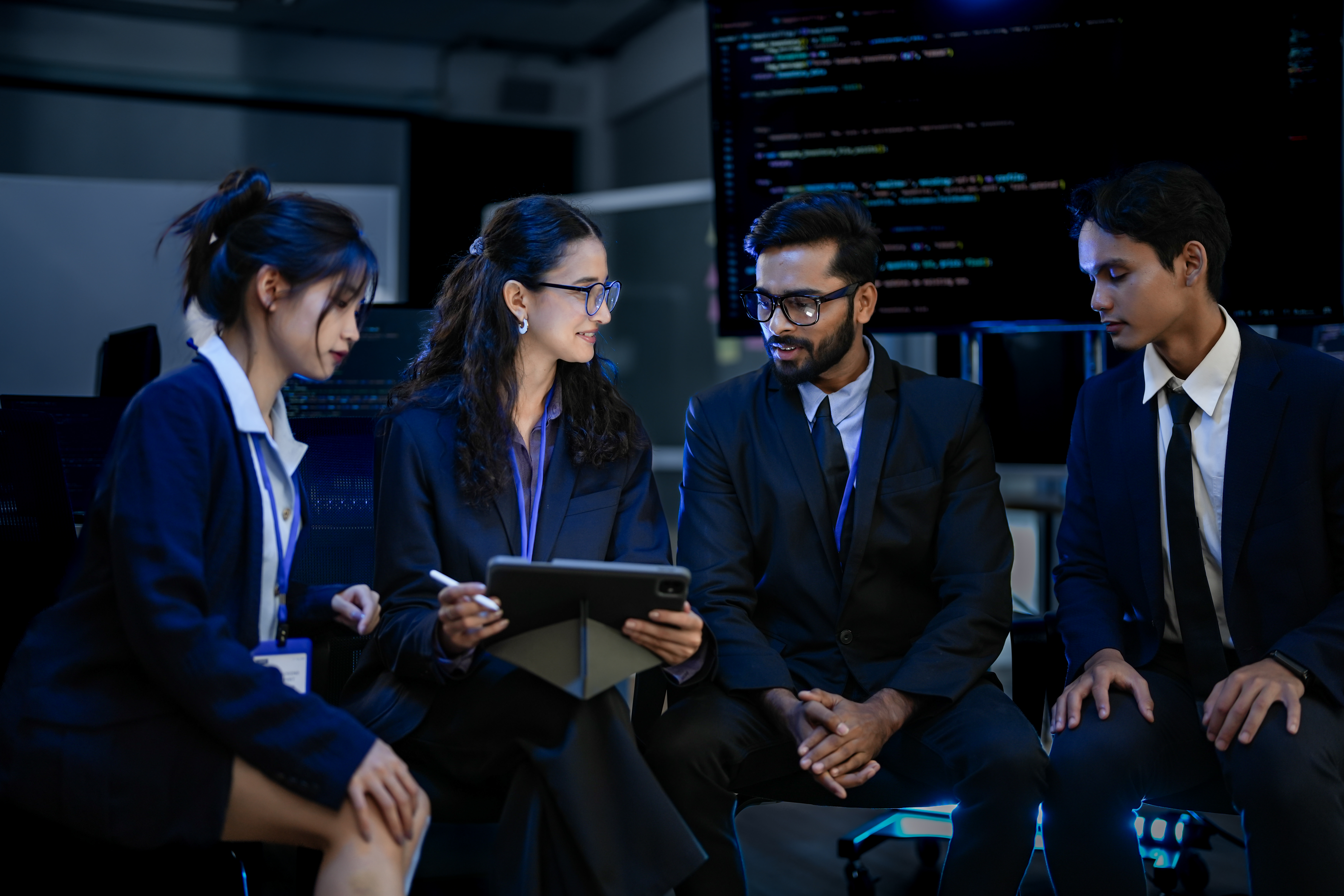 A Development Team Participates In A Project Debriefing In A Corporate Command Center They Are Analyzing Post Launch Metrics And Discussing The Next Development Sprint And Strategy