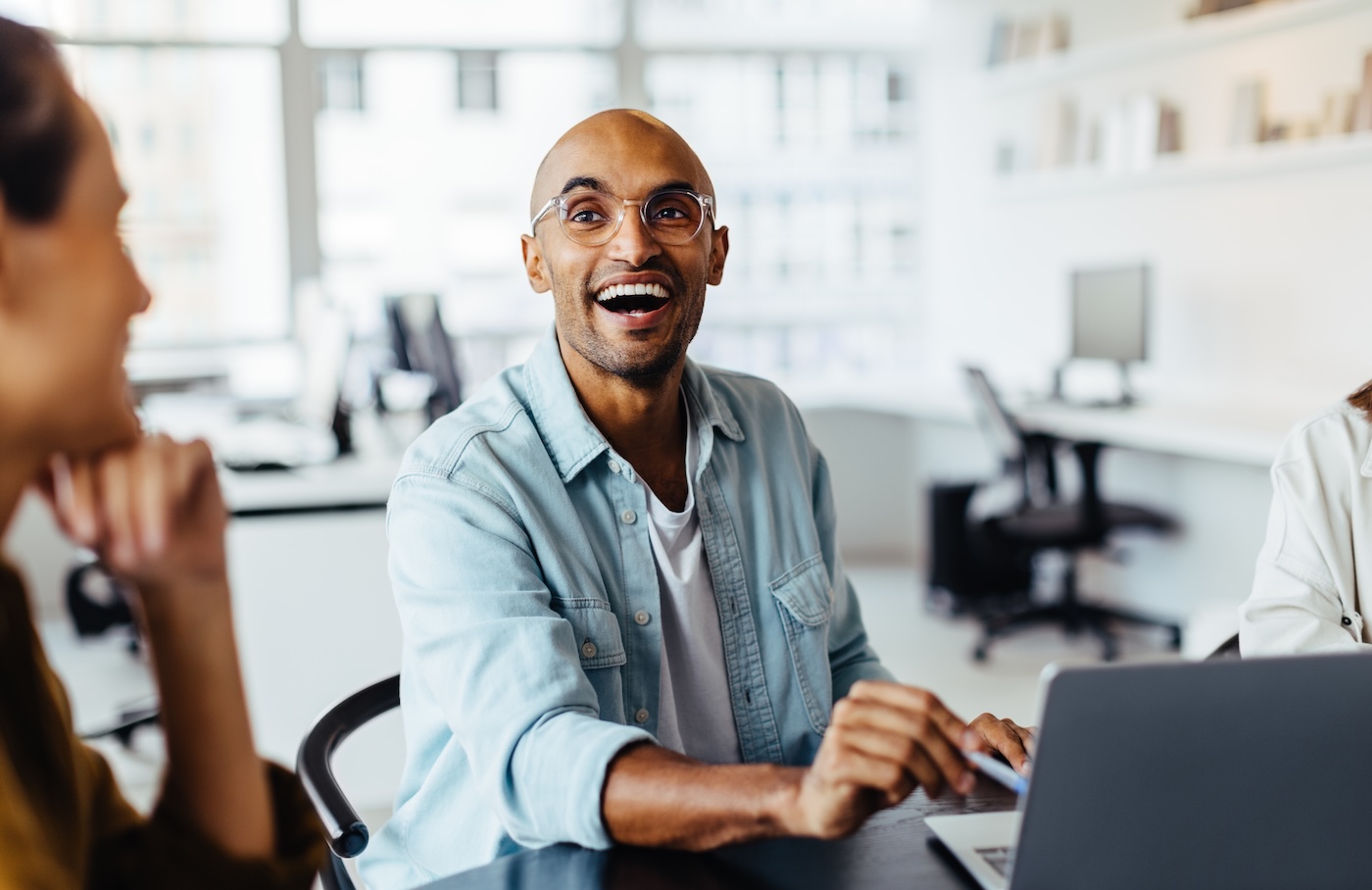 Male designer discussing a new project with his team in an office. Black business man using a laptop while sitting at a meeting table with his colleagues.