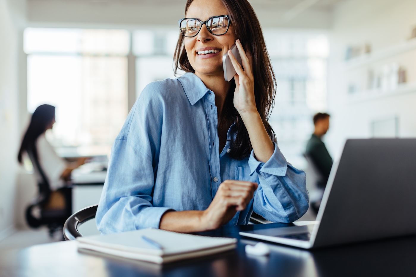 Female business professional making a phone call while sitting in an office. Business woman working with a laptop in a co-working office.