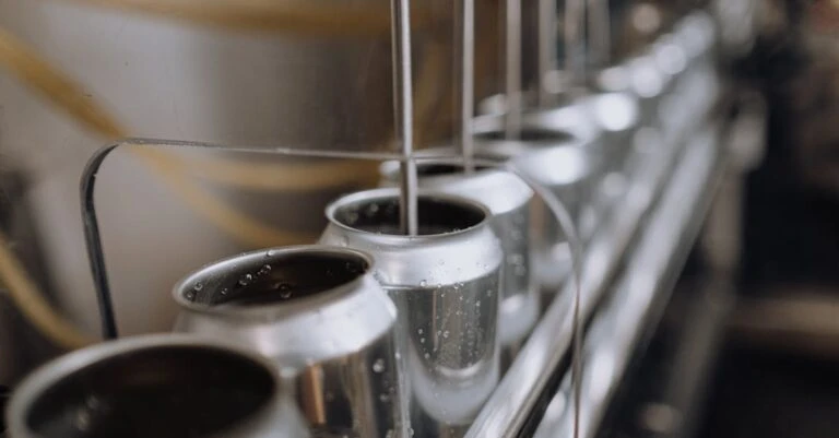 Open metal cans aligned beneath filling nozzles on a production line.