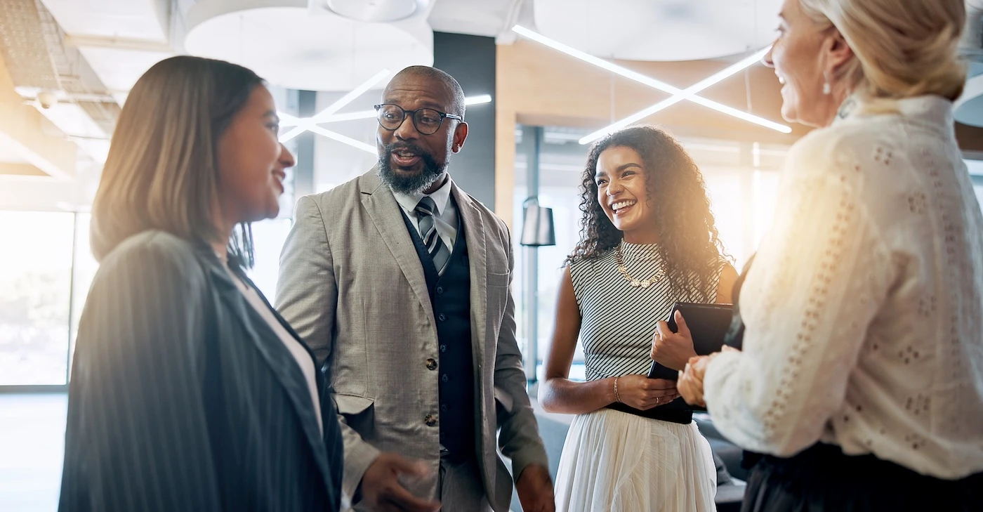 People smile and talk while standing together in a sunlit office.