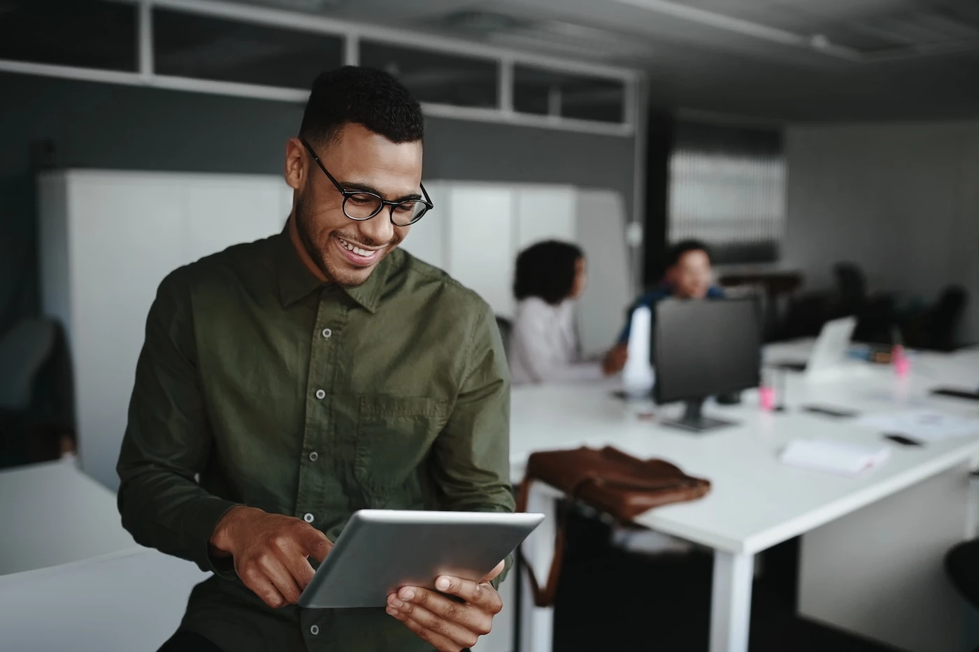 Successful smiling young man in office using digital tablet