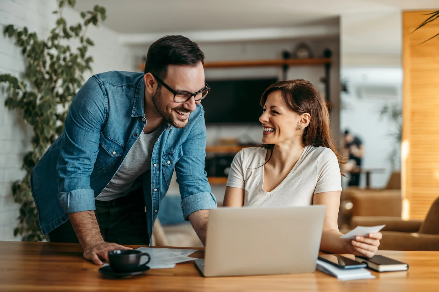 Great results! Portrait of a beautiful smiling woman sitting at desk with laptop and her coworker standing and looking at it, in the office.