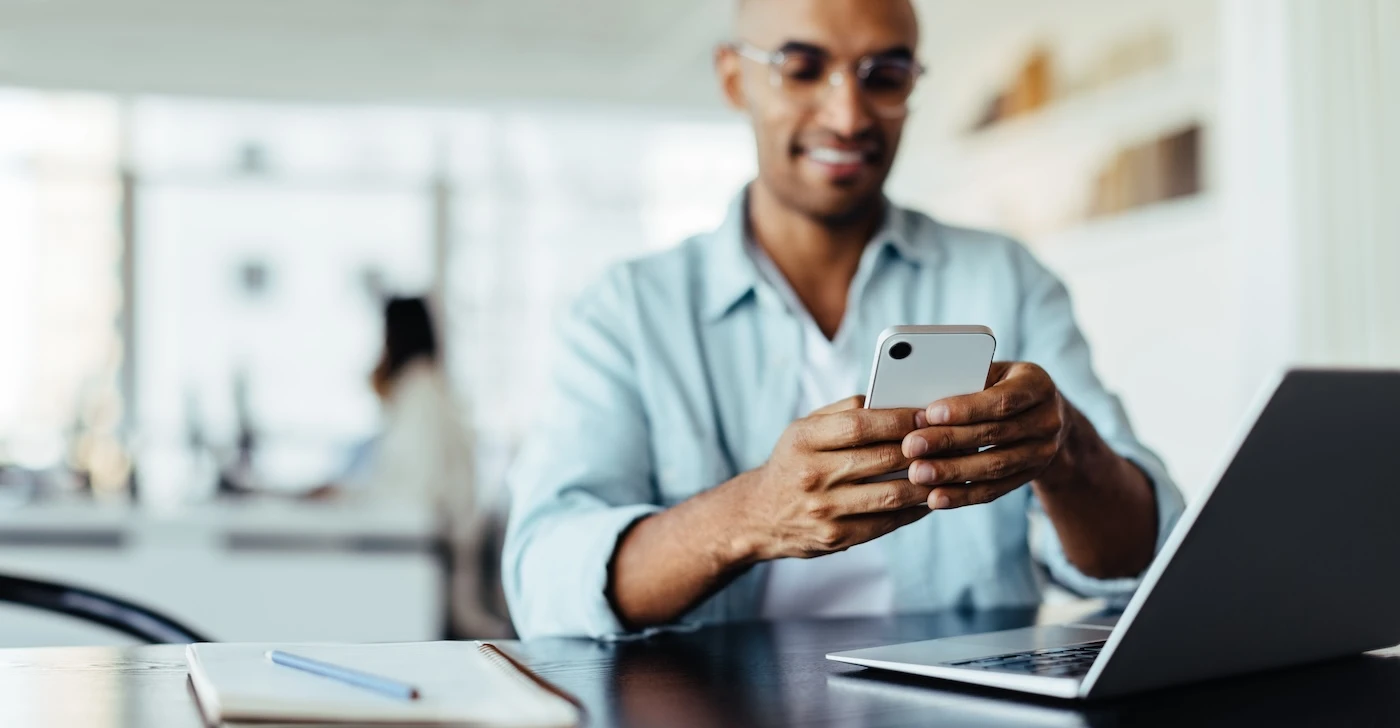 Black business man sitting in an office and using a smartphone. Happy young man working in digital marketing.