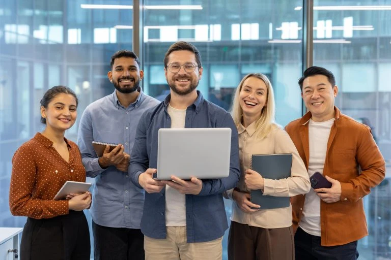 A diverse, happy team of professionals gathered together, smiling for a team photo in the office.