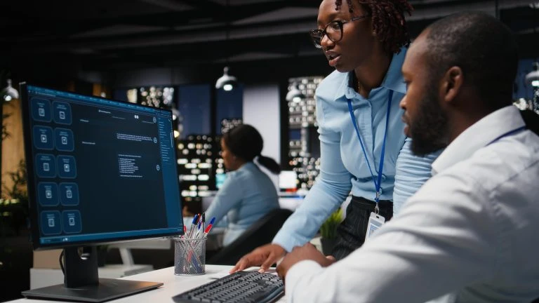 Two black workers interacting with a virtual assistant on computer at desk